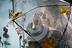 Sad woman wipes tears under a transparent umbrella with raindrops with autumn leaves. Soft focus