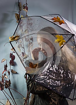 Sad woman wipes tears under a transparent umbrella with raindrops with autumn leaves. Soft focus