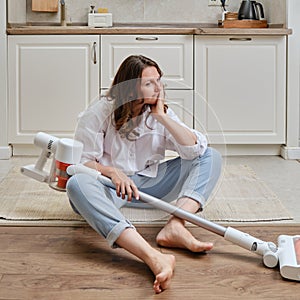 A sad woman with a wireless portable vacuum cleaner in the kitchen. A