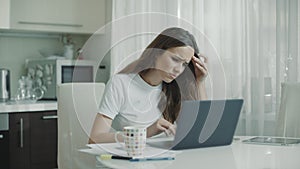 Sad woman working laptop at white kitchen. Unhappy person use computer