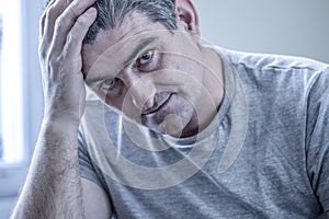 Sad and worried man with grey hair sitting at home couch looking photo