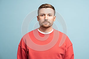 Sad worried man with serious face expression stands looking at camera on blue background in studio