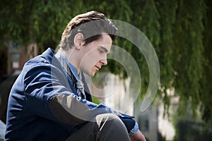 Sad, worried young man sitting outdoor in town