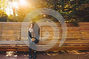 Sad young afro-haired woman sit alone on a wooden bench in autumn park at sunny warm day. Portrait of alone woman