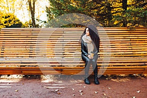 Sad young afro-haired woman sit alone on a wooden bench in autumn park at sunny warm day. Portrait of alone woman