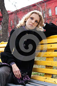 Sad young blonde sitting on a bench in the park