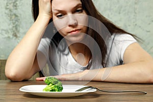Sad young brunette woman dealing with anorexia nervosa or bulimia having small green vegetable on plate. Dieting problems, eating photo