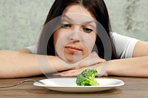 Sad young brunette woman dealing with anorexia nervosa or bulimia having small green vegetable on plate. Dieting problems, eating photo