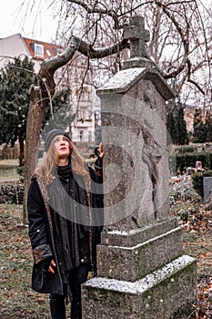 Sad young brunette woman standing on snowy day next to grave