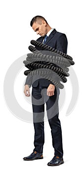 A sad young businessman stands tightly bound by large phone cords on a white background.