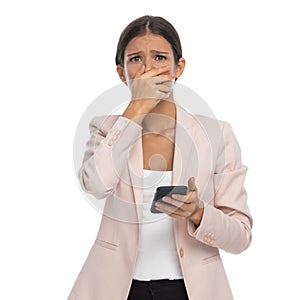 Sad young businesswoman covering mouth with hands and reading texts