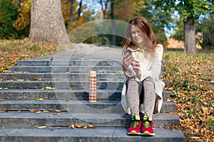 Sad young caucasian woman looking at mobile phone on the stairs outdoors