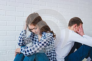 Sad Young couple is sitting back to back on the couch at home having a quarrel