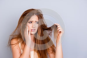 Sad young cute girl is looking at her damaged hair with shock, s