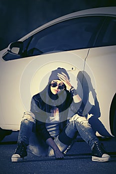 Sad young fashion woman in sunglasses sitting next to her car
