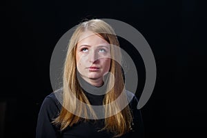 Sad young girl blonde hair crying on a black background.