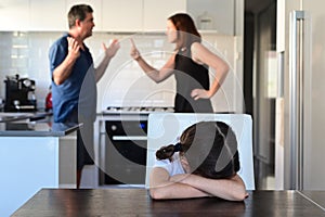 Sad young girl covering her face while parents arguing in home kitchen