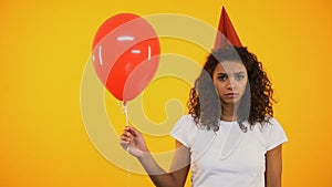 Sad young girl holding red balloon, upset and lonely on birthday celebration