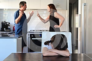 Sad young girl covering her face while parents arguing in home kitchen photo