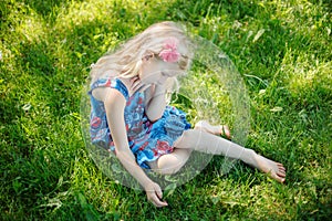 Sad young girl sitting on ground outdoor on summer sunny day. Pensive little child dreaming thinking. Insecure lonely kid trying