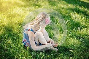 Sad young girl sitting on ground outdoor on summer sunny day. Pensive little child dreaming thinking. Insecure lonely kid trying