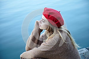 Sad young girl sitting on the pier, thoughtful, lonely