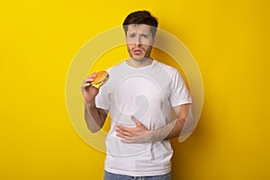 Sad Young Guy Holding Burger Suffering From Stomachache