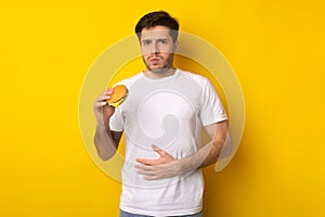 Sad Young Guy Holding Burger Suffering From Stomachache