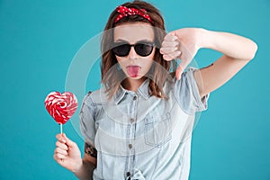 Sad young lady eating candy and showing thumbs down.