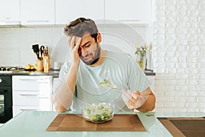 Sad young man look longingly at salad hold fork with greens in hand plate salad in front of him. photo