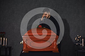 Sad young man near funeral casket with red rose