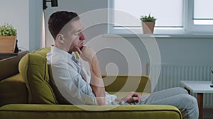 Sad young man is sitting on the sofa at home. The depressed male sitting at home on the sofa.