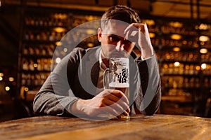 Sad young man in a suit looking at a glass of beer while sitting at a table in a pub. A man drinks after work in a pub.