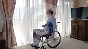 Sad young man in wheelchair looking through the window