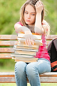 Sad young student girl sitting on bench with books