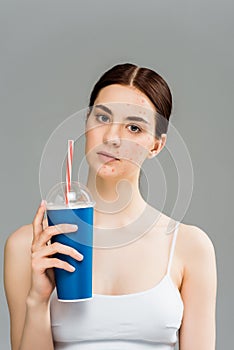 Sad young woman with acne on face holding plastic cup