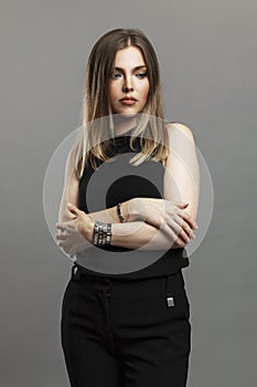Sad young woman. A beautiful blonde woman in black clothes in a closed pose is standing. Depression and stress. Gray background.