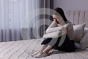 Sad young woman on bed at home, space for text. Loneliness concept