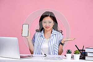 Sad young woman business worker in a casual shirt sitting at a desk with a PC She is holding a blank screen smartphone and