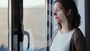 Sad young woman crying while looking through the window at home.