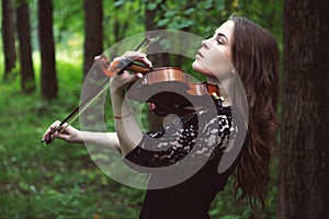 Sad young woman enthusiastically playing the violin romantic work in the Park among the trees