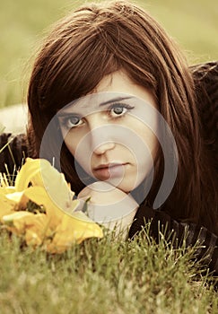 Sad young woman with a flowers lying on the grass