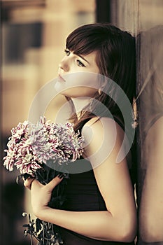 Sad young woman with a flowers standing at the wall