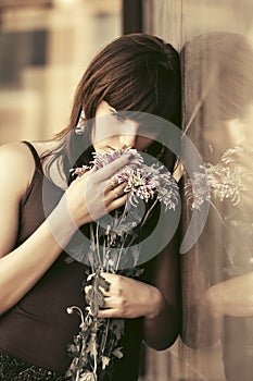 Sad young woman with a flowers standing at the wall