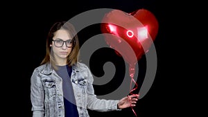 Sad young woman let go of heart-shaped balloon. A sad woman stands with helium balls on a black background. Valentine`s