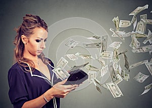 Sad young woman looking at her wallet with money dollar banknotes flying out away photo