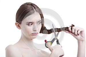 Sad young woman with scissors cutting her hair over white background