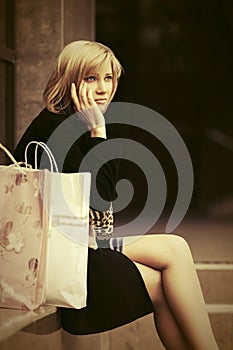 Sad young woman with shopping bags sitting on steps