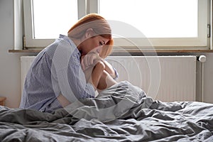 sad young woman sitting on bed suffering from loneliness and depression