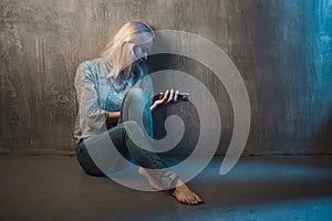 Sad young woman sitting on the floor with a phone in hands. Call waiting, no connection.